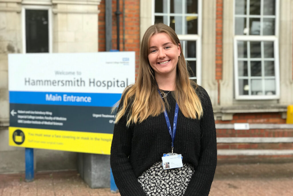 Image of a smiling woman standing in front of a sign that reads "Hammersmith Hospital" 