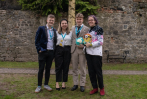 Image of 4 people standing on grass smiling at the camera