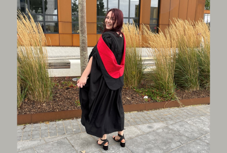 Image of a person wearing a graduation gown, smiling at the camera